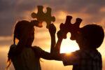 shillouette of two children holding large puzzle pieces